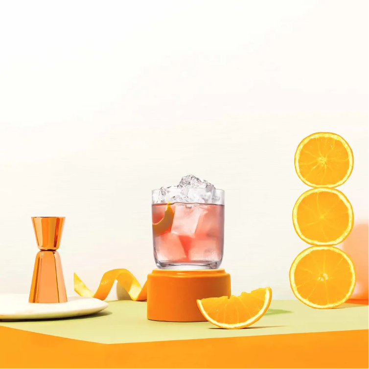 Jasmine Cocktail on ice with orange wheels, wedge, and orange zest, plus shot glass