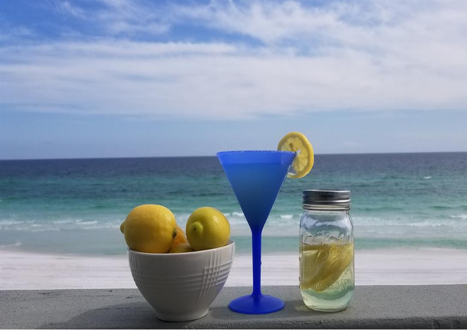 bowl of lemons, blue martini glass, and mason jar with lemon wheels on a beach with ocean view