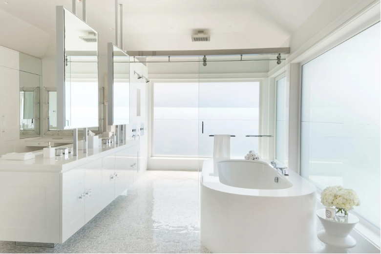 sparkling clean beach home bathroom with glossy white finishes, soaking tub, twin vanities, and mirrors with spectacular ocean views