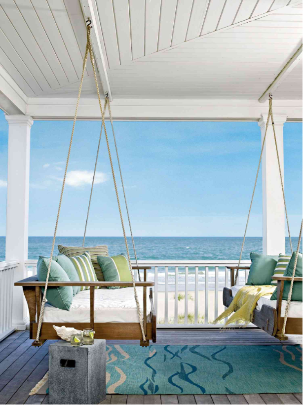 Swinging daybeds on a beachfront covered porch with white washed railing and ceiling