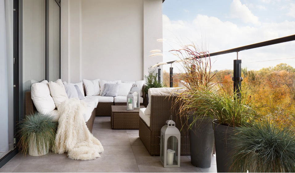 beachfront outdoor balcony with glass railing, wicker sectional, lanterns, metal planters, and white cushions, furry throw