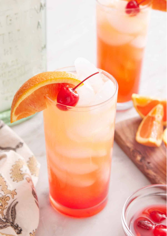 Tequila Sunrises in tall glasses filled with ice and garnished with orange slices and maraschino cherries.