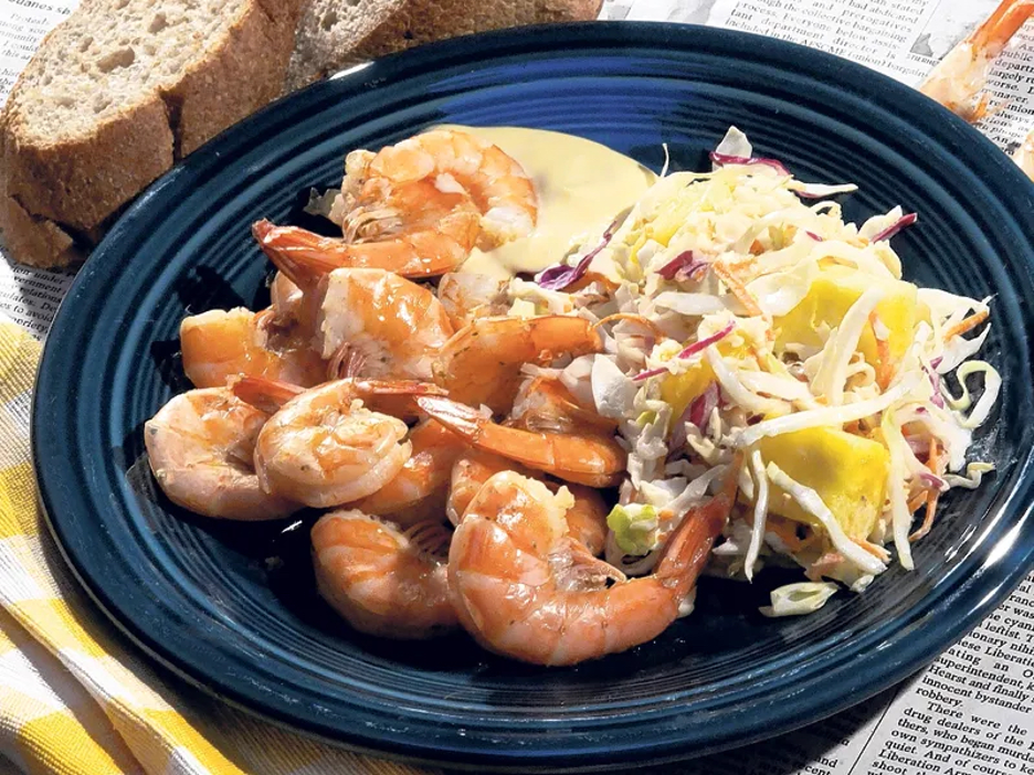 Key West Shrimp Boil served on blue plate on top of newspaper with tropical coleslaw and pieces of baked bread