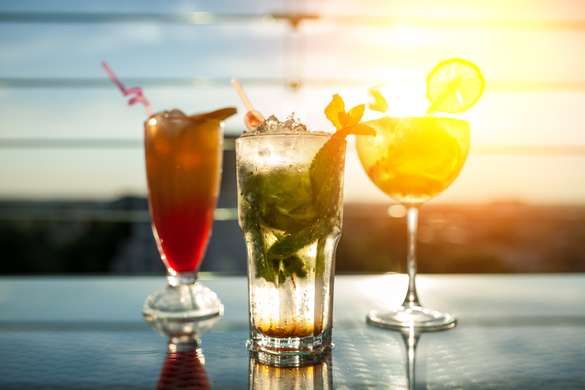 Hero shot of three cocktails with an ocean sunset in the backdrop.