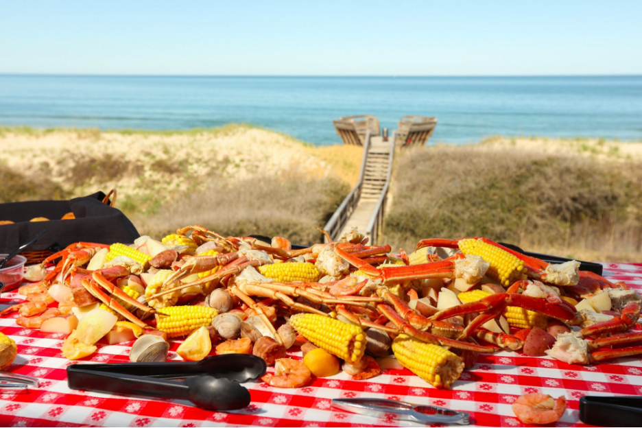 Seaside Seafood Bolil spread over a plastic table cloth and an ocean view in the backdrop with a boardwalk bridge