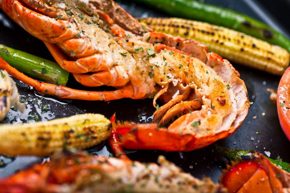 Grill Lobster with Lemon-Chive Butter Sauce cooking on a grill pan with charred corn-on-the-cob, and other vegetables