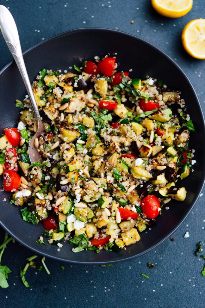 Meditarranean Quinoa Salad with Roasted Vegetables in a skillet with lemon wedges in background