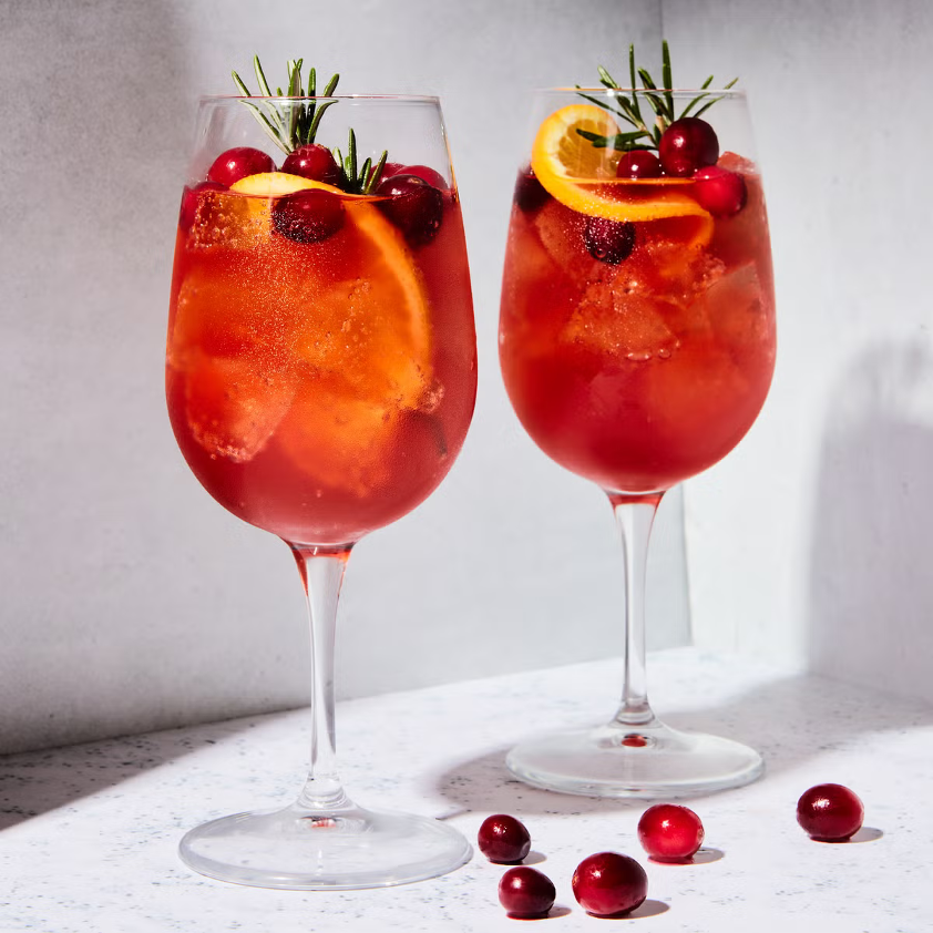  Cranberry-Aperol Spritzes in wine goblets garnished with cranberries, orange slices, and fresh rosemary sprigs.