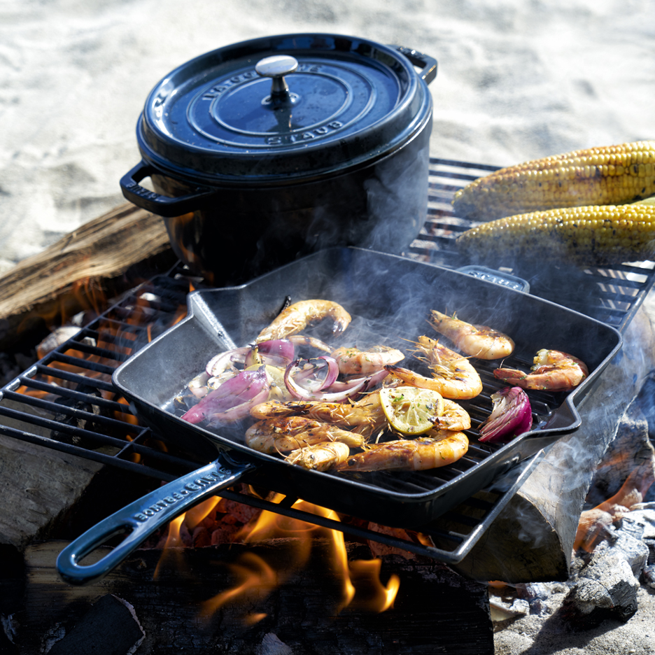 Grilled Shrimp in a cast-iron grill pan roasting on grate at a beach bonfire with charred corn-on-the-cob