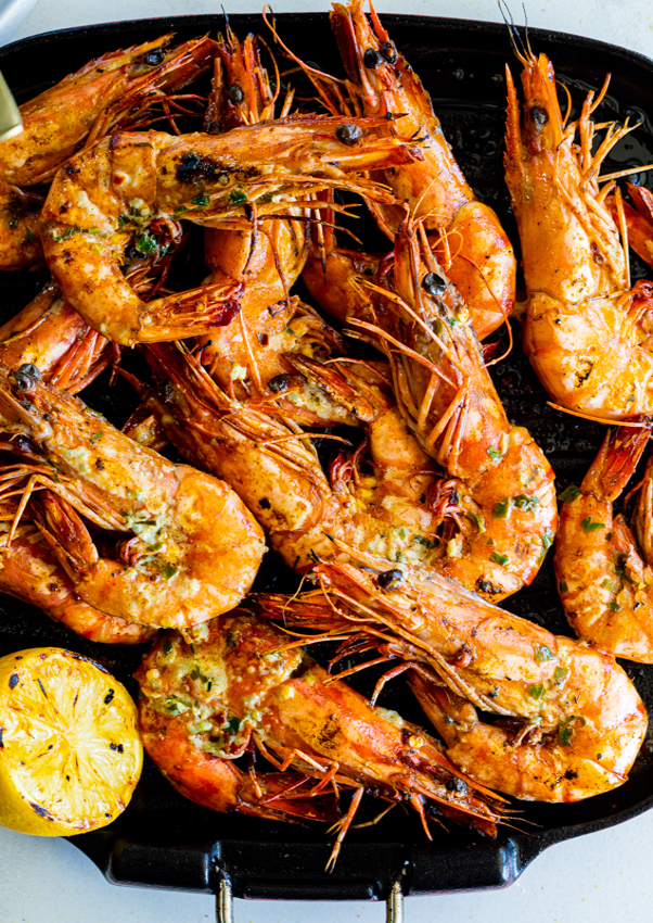 Grilled Garlic Butter Prawns with shells on in a grill pan with a grilled halved lemon