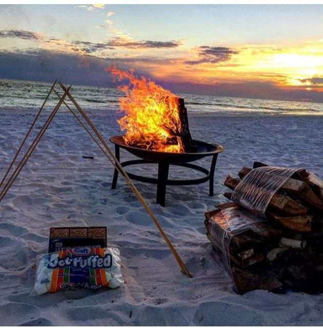 Beach bonfire on the sand on the gulf coast in Florida with an ocean backdrop during sunset and bundles of firewood and s'mores kit in the foreground