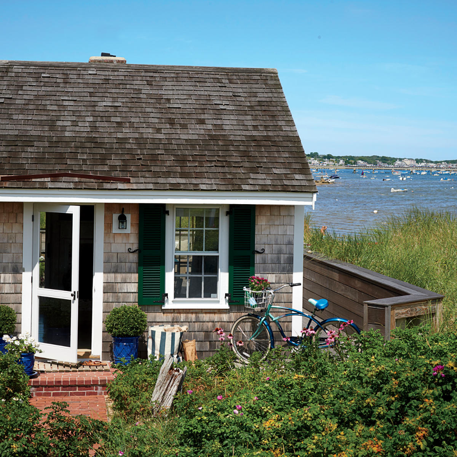 exterior shingled beach cottage in New England area with boats on the ocean in background, bicycle out front 