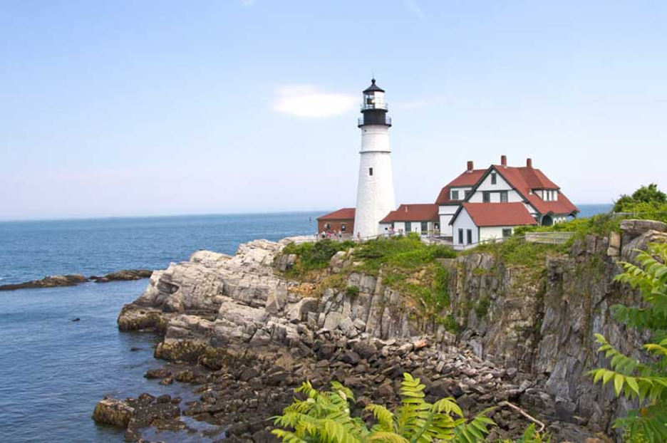 New England rocky coastline with white lighthouse, ocean in backdrop, and natural greenery and coastal scenery