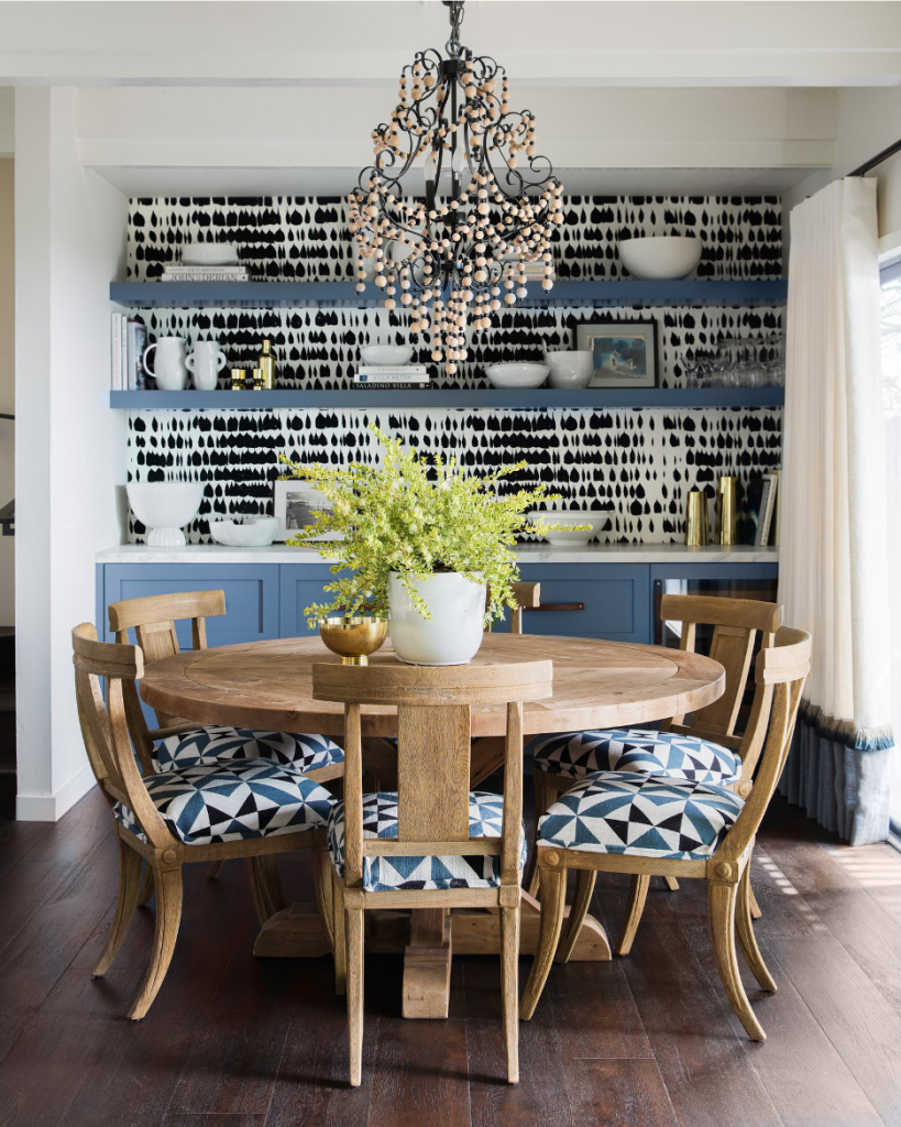 Small coastal dining room with round table, upholstered seating, and built-in cabinetry with open shelving, bead chandelier