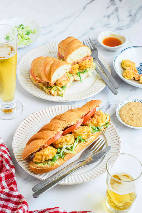 Shrimp Po'Boy Sandwiches on plates with remoulade sauce and glasses of beer in the background