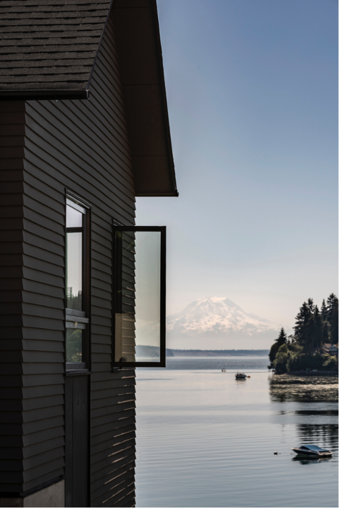 Side exterior of gabled beach home overlooking waters of Puget Sound and Mount Rainer. House window open to the fresh air