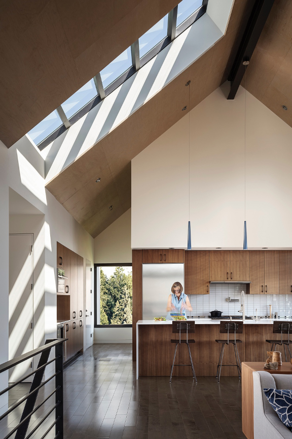 Home House kitchen with huge skylight casting shadows on the walls and ceiling. Homeowner's wife in kitchen preparing food. 