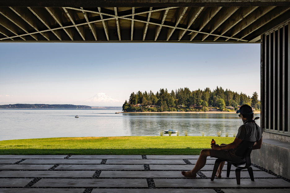 Lower level covered patio with views of Puget Sound and the water. Homeowner sitting on chair relaxing.