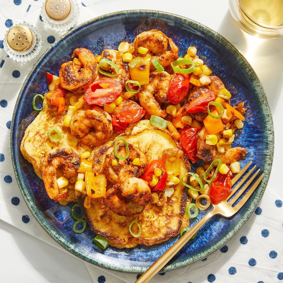 Cajun Shrimp & Corn Pancakes on a blue plate topped with tomatoes, sweet corn, scallion ribbon, and sweet peppers.