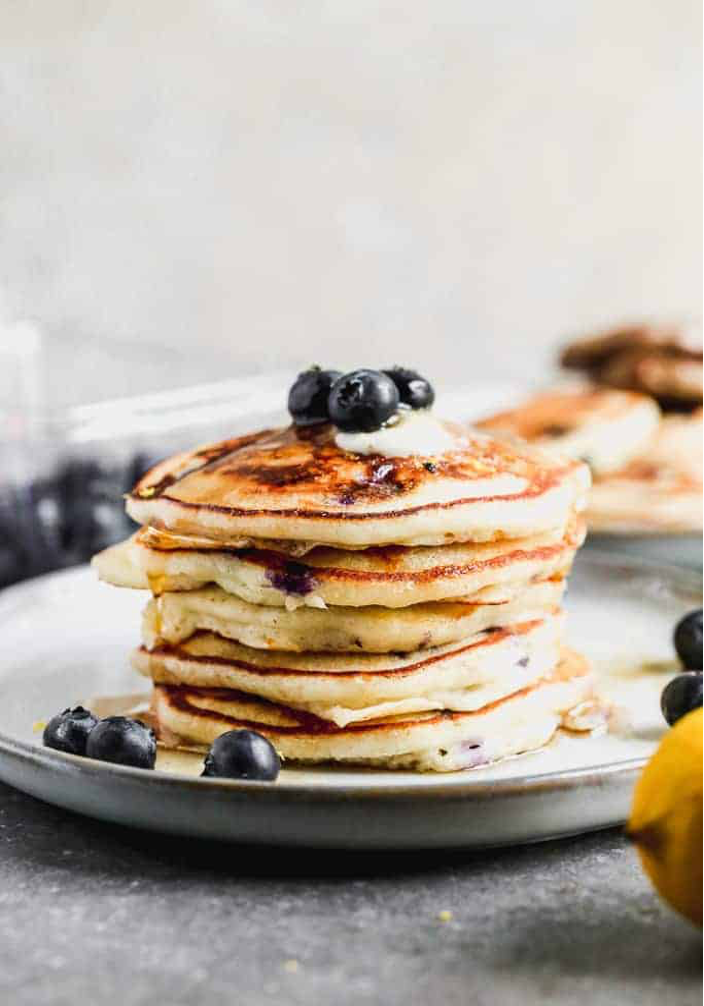 Stack of Lemon and Blueberry Pancakes on a plate garnished with blueberries and a whole lemon in the foreground