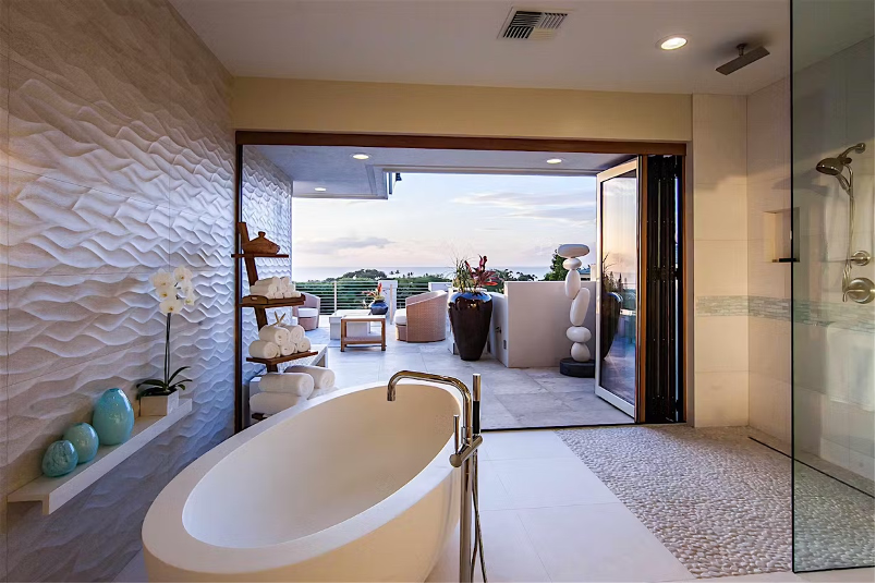 Biophilic design elements demonstrated in this open and airy beach home bathroom that connects to the outdoor spaces and ocean, spotlighting a luxurioous soaking tub and pebble-paved shower area.