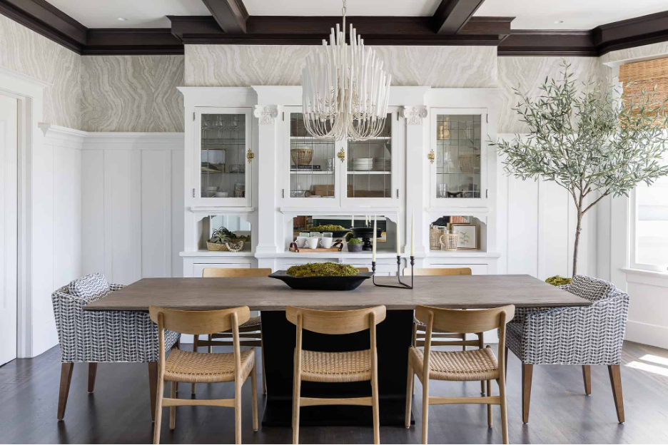 Bold statement lighting demonstrated in a beach home dining room with a stunning white candelabra chandelier hanging from tray ceiling with dark wood embellishments