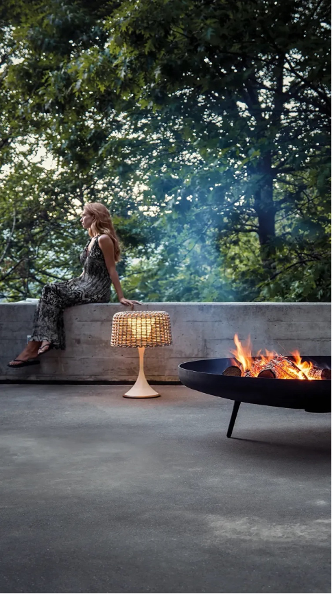 Outdoor firebowl and lamp from Gloster on a patio with a woman in background