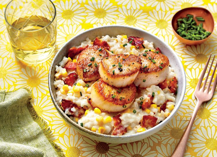 Lowcountry Creamy Rice with Scallops served in large bowl with glass of white wine and green garnish in background