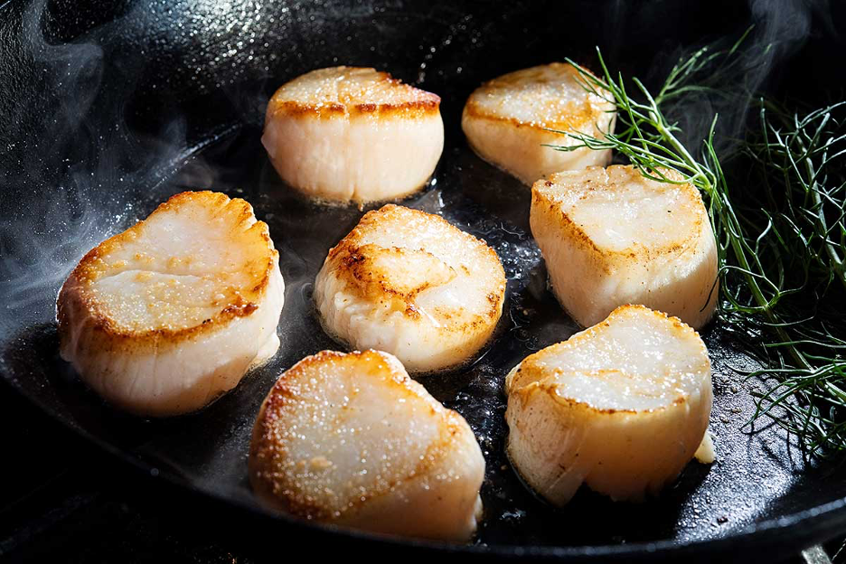 Seared fresh sea scallops in an iron skillet with rosemary herbs on the side